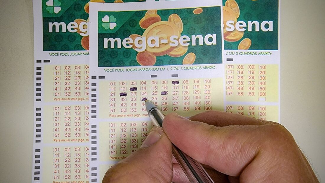 Mão segura caneta sobre volantes da Mega-Sena
