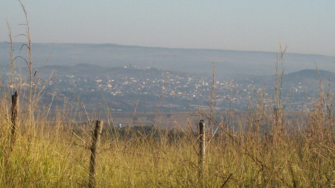 Vista distante da cidade de Santo Antônio do Descoberto, com capim alto e cerca em primeiro plano e morros ao fundo