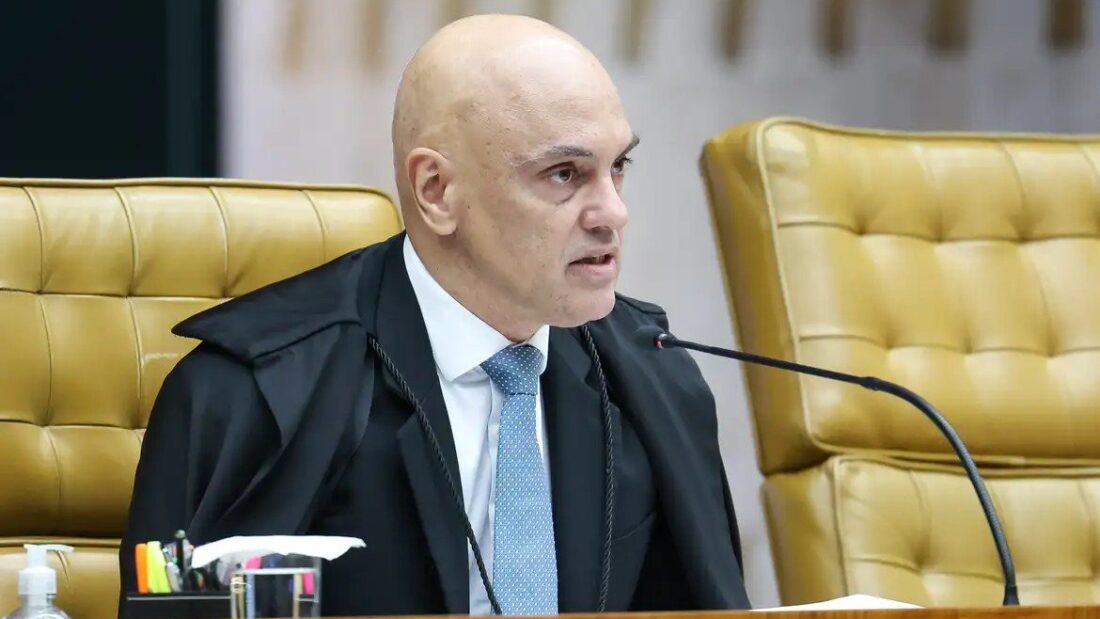 Ministro Alexandre de Moraes, de toga, fala ao microfone sentado em poltrona amarela no plenário do Supremo