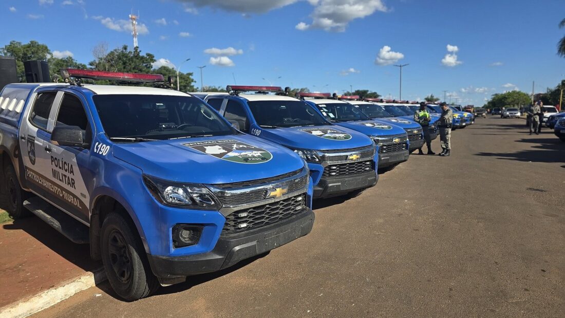 Fila de caminhonetes azuis da Polícia Militar de Goiás estacionadas em uma avenida