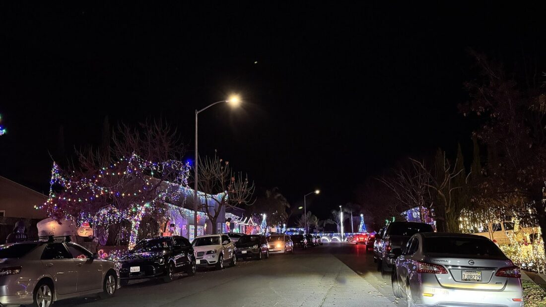 Rua à noite com casas e árvores enfeitadas com luzes de Natal coloridas e carros estacionados