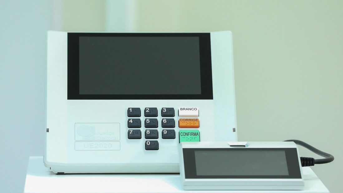 Urna eletrônica brasileira modelo UE2020 e terminal do mesário sobre uma mesa branca