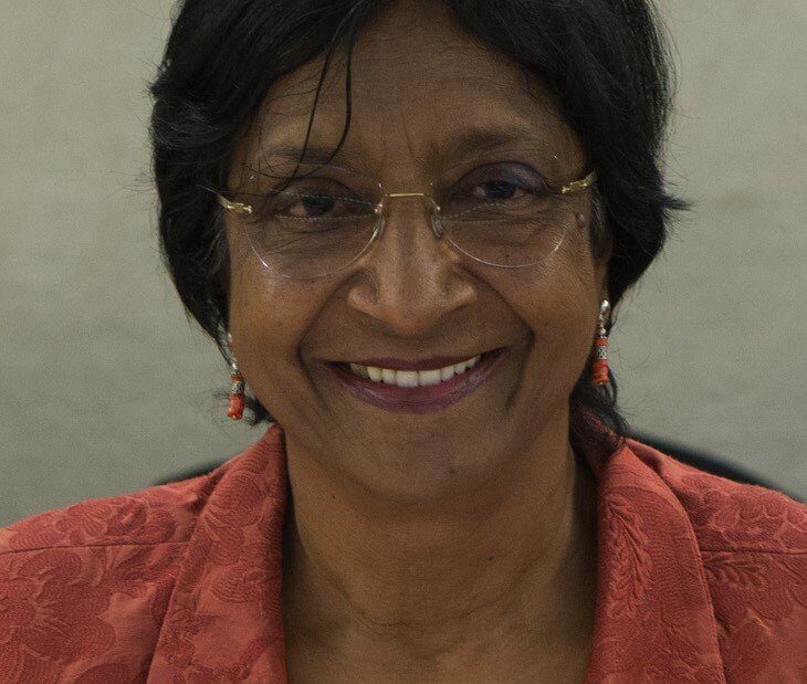 Navi Pillay, de cabelos curtos escuros, óculos e blazer coral, sorri para a câmera