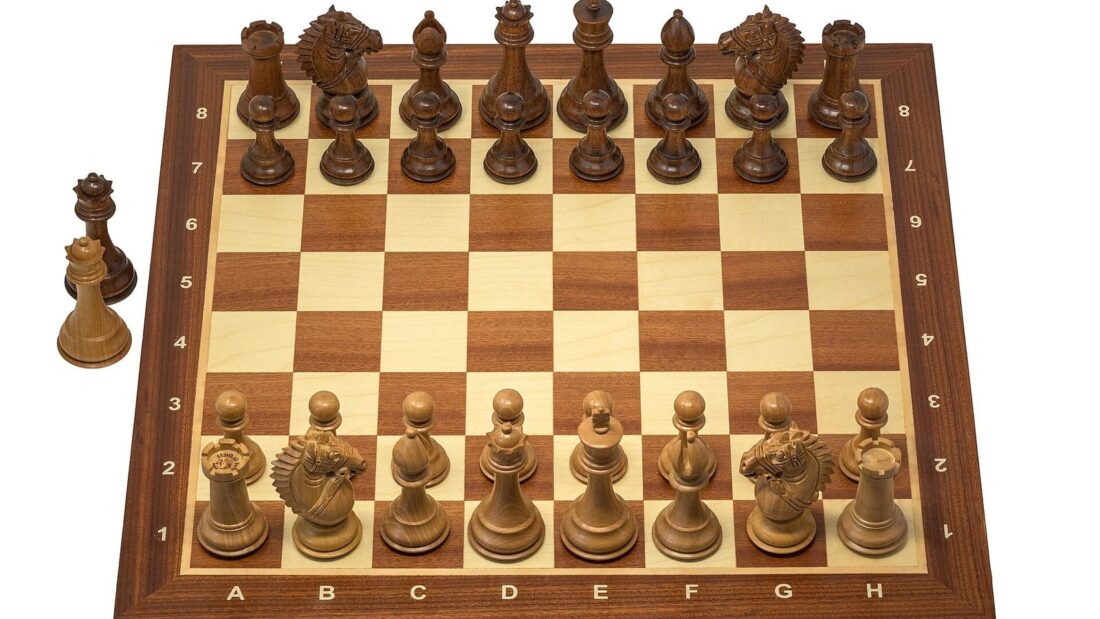 Tabuleiro de xadrez de madeira com as peças de madeira clara e escura arrumadas na posição inicial