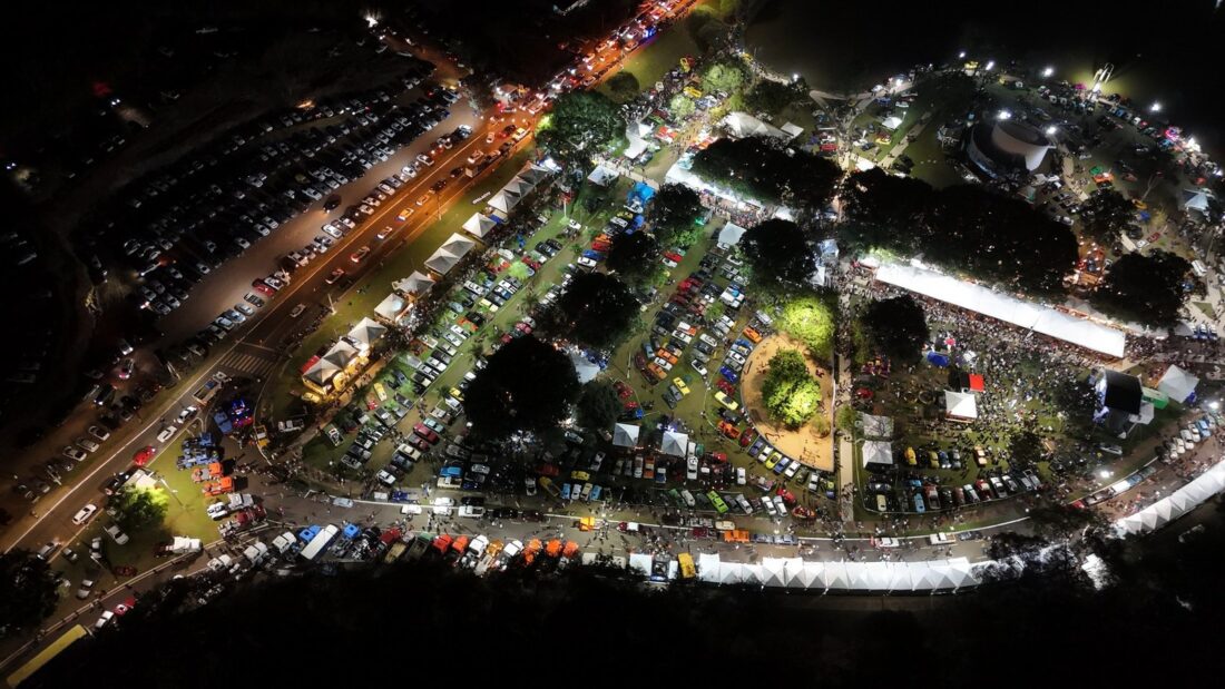 Vista aérea noturna do Lago JK, em Jataí, com tendas, palco iluminado e muitos carros estacionados ao redor durante um evento