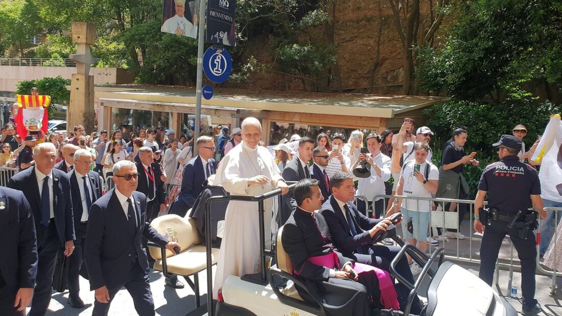 Papa Leão XIV, de batina branca, acena de um papamóvel aberto cercado por seguranças e fiéis