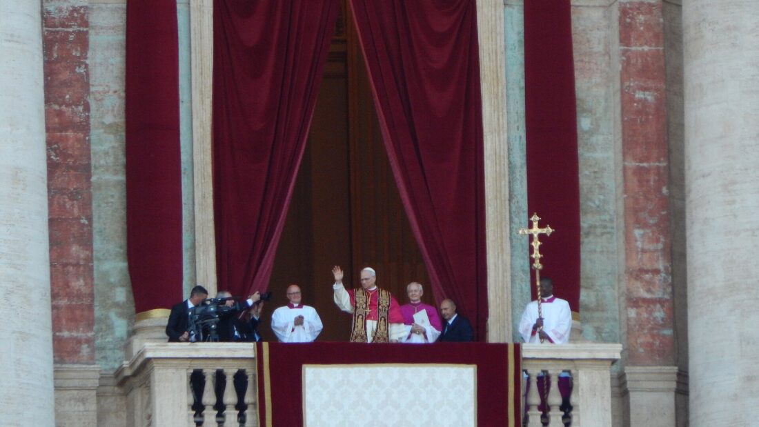Papa Leão XIV acena do balcão central da Basílica de São Pedro, cercado por religiosos