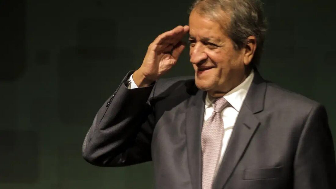 O presidente do PL, Valdemar Costa Neto, de terno, faz continência e sorri durante entrevista