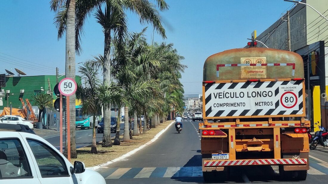 Avenida Presidente Vargas, em Rio Verde, com carros, uma moto e um caminhão bitrem trafegando entre palmeiras