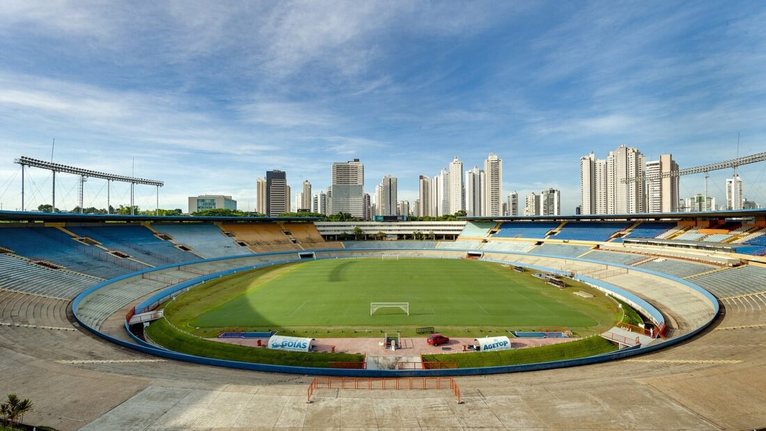 Vista interna do Estádio Serra Dourada, com gramado, arquibancadas e prédios de Goiânia ao fundo
