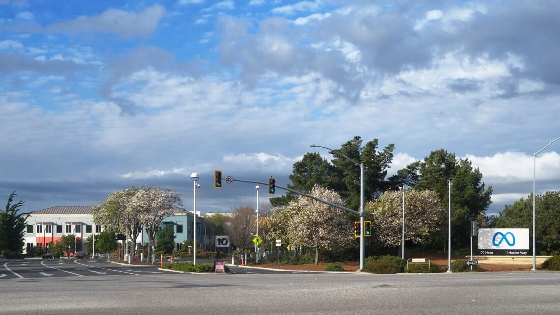 Avenida com semáforo e, ao fundo, a placa azul com o símbolo da Meta na entrada da sede da empresa