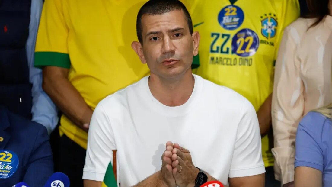 Douglas Ruas, de camiseta branca, fala a microfones de emissoras cercado por apoiadores com camisas amarelas