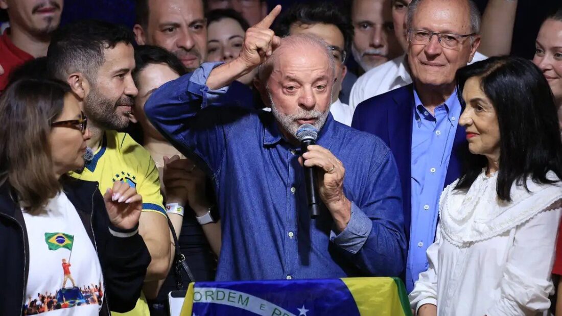Lula fala ao microfone com o dedo indicador levantado, cercado por aliados, entre eles Geraldo Alckmin