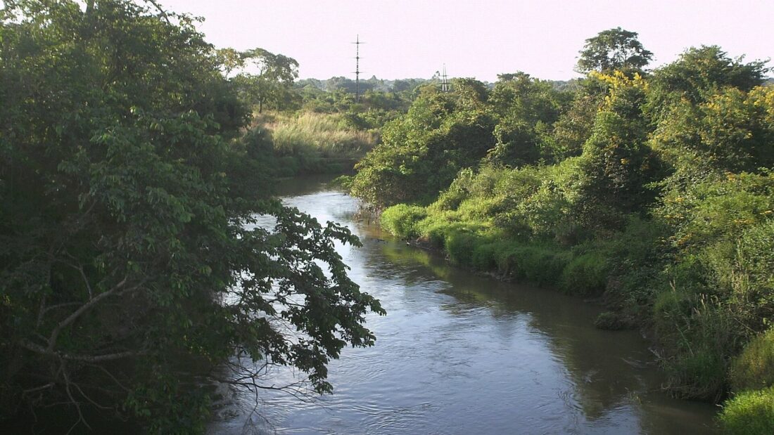 Trecho do Rio Meia Ponte em Goiânia, de águas escuras e calmas, cercado por mata densa nas duas margens