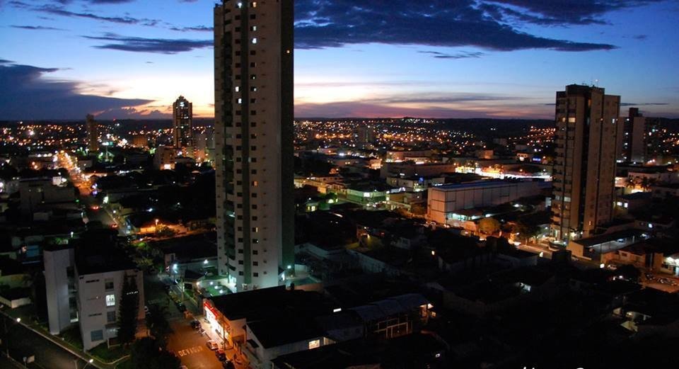 Vista noturna do centro de Rio Verde, com prédios altos iluminados e o céu do entardecer