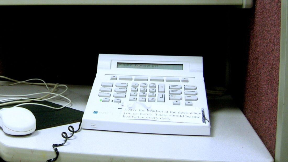 Aparelho telefônico de central de atendimento sobre uma mesa de escritório, ao lado de um mouse