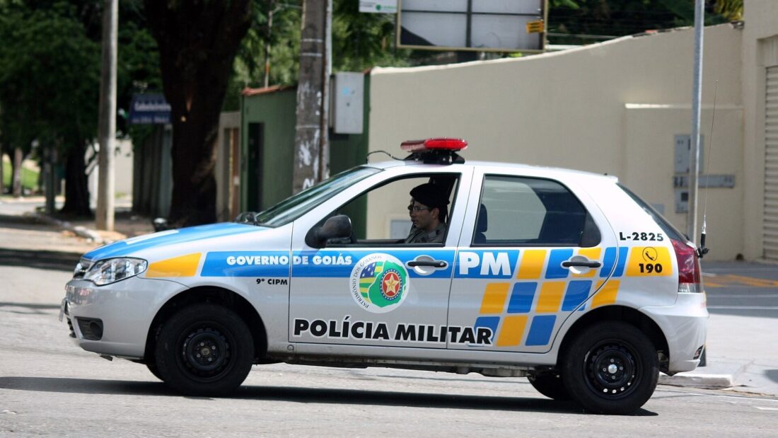 Viatura branca da Polícia Militar de Goiás, com faixas azul e amarela, trafega em rua de Goiânia