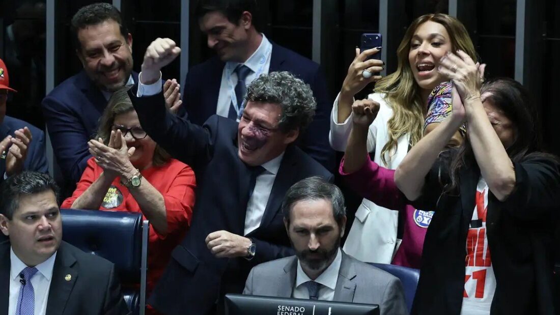 Senadores e senadoras comemoram no plenário do Senado, com punhos erguidos e celulares na mão, ao lado de uma pessoa com camiseta vermelha da campanha pelo fim da escala 6x1