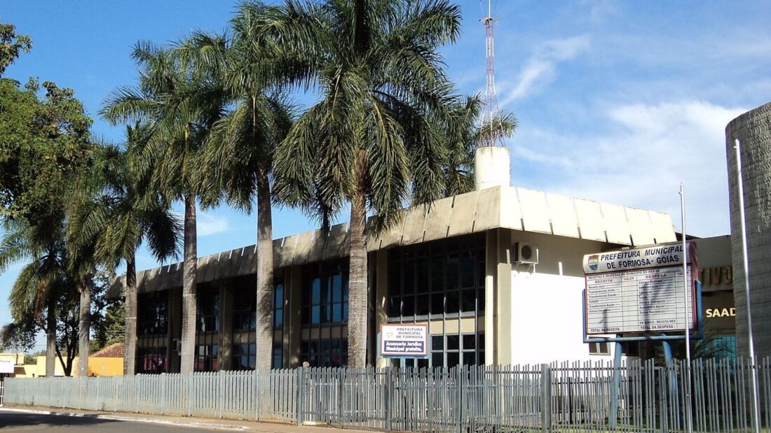 Prédio da Prefeitura Municipal de Formosa com fachada bege, palmeiras à frente, grade e uma placa com o nome da prefeitura e um quadro de receitas e despesas