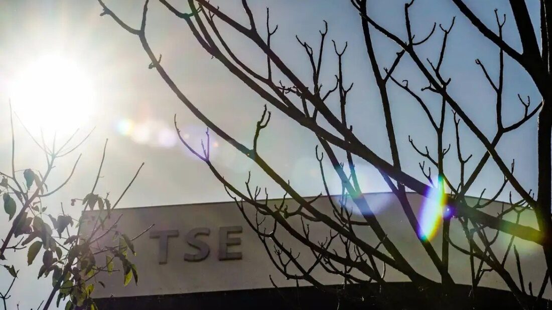 Letreiro com a sigla TSE na fachada do Tribunal Superior Eleitoral, em Brasília, visto entre galhos secos de árvore, com o sol ao fundo