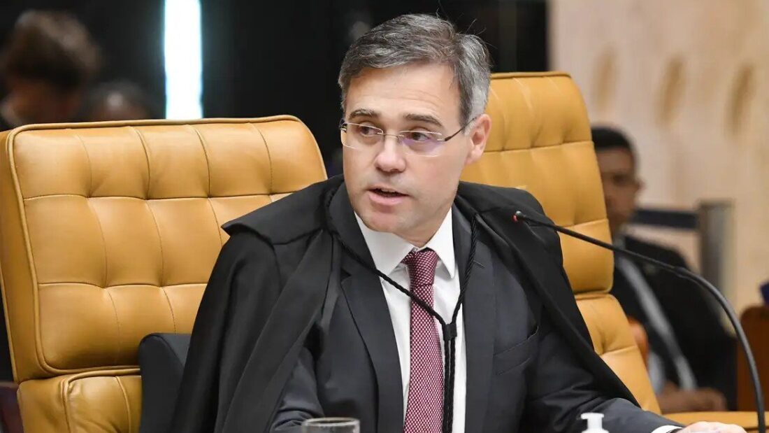 Ministro André Mendonça, de toga, fala ao microfone sentado em poltrona amarela durante sessão plenária