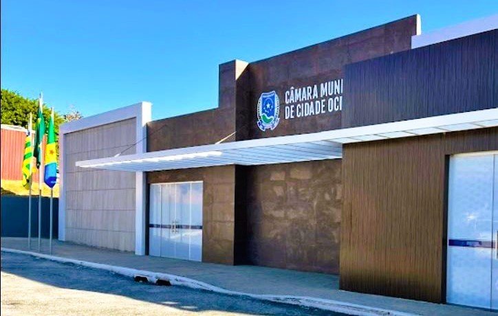 Fachada da Câmara Municipal de Cidade Ocidental, prédio moderno com revestimento escuro e marquise, com bandeiras hasteadas à esquerda