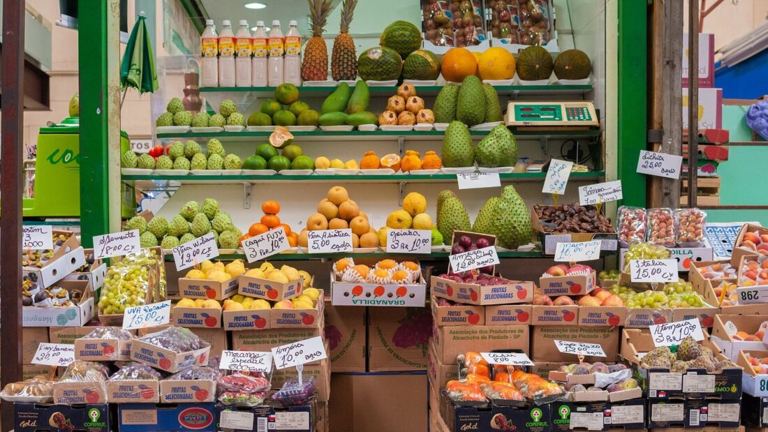 Box de frutas de um mercado municipal, com caixas de frutas empilhadas até o teto e etiquetas de preço