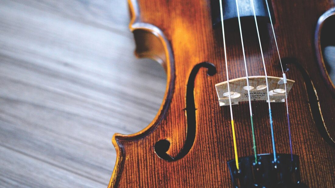 Detalhe de um violino de madeira escura, com as cordas e o cavalete em primeiro plano