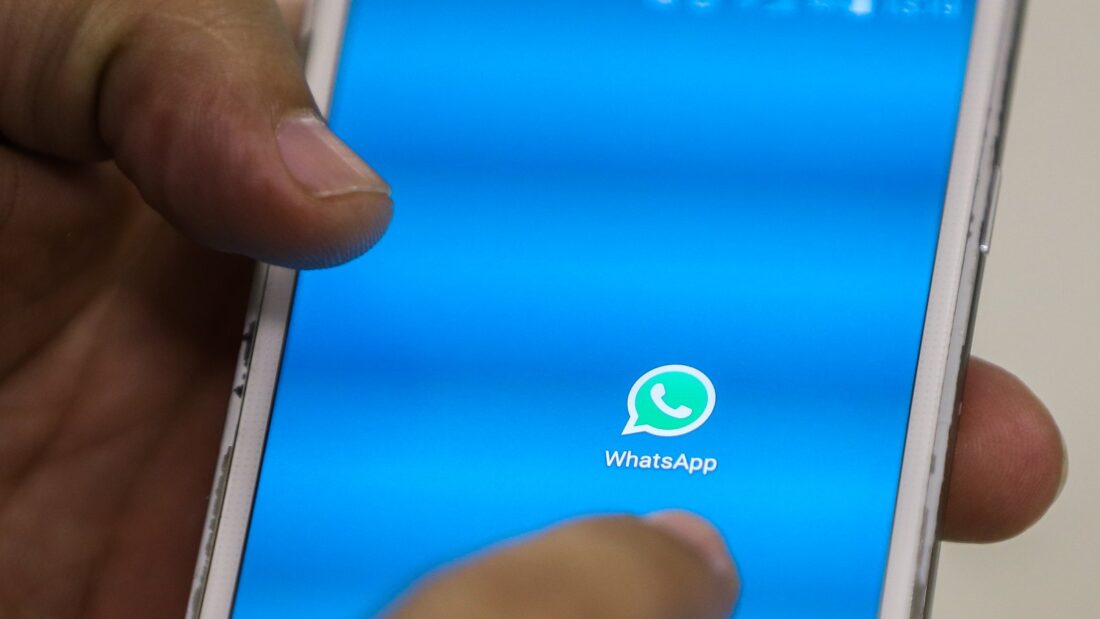 Mão segura celular com a tela de abertura do WhatsApp